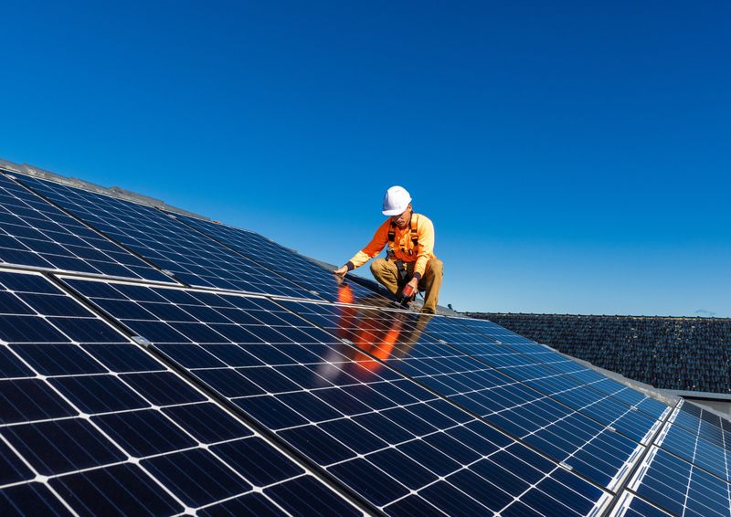 Instalador fixando módulos solares em um telhado sob céu azul